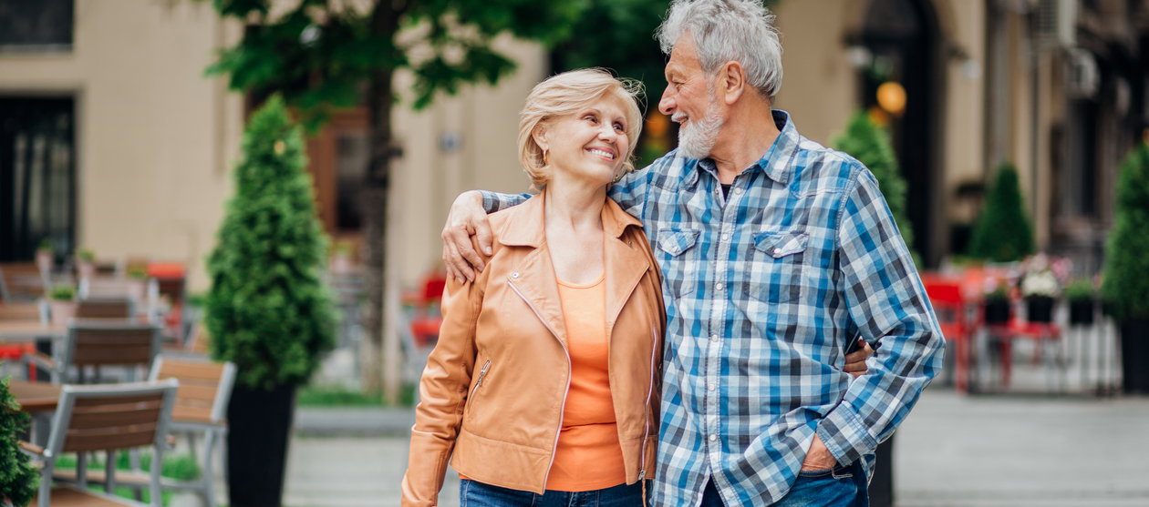 Opa (rechts) und Oma (links vorne) gehen Arm in Arm spazieren.